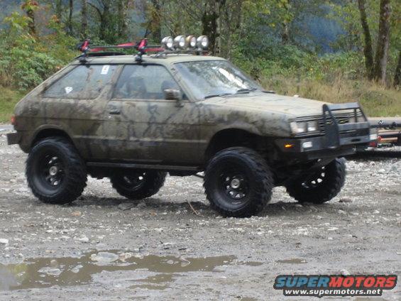Lifted Subaru hatchback with off-road tires and roof lights, parked on a dirt road