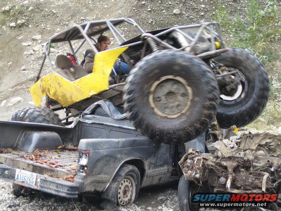 Off-road buggy on top of a pickup truck, with a driver visible