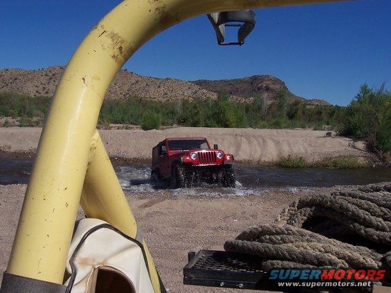 Red Jeep Wrangler driving through a river. Shot from inside another vehicle