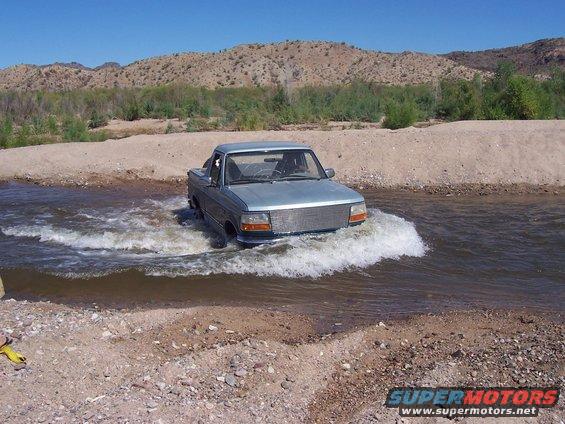 Light blue pickup truck with a large chrome grille driving through water