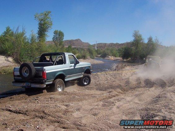 1996 Ford Bronco and another off-road vehicle crossing a river on a dirt path