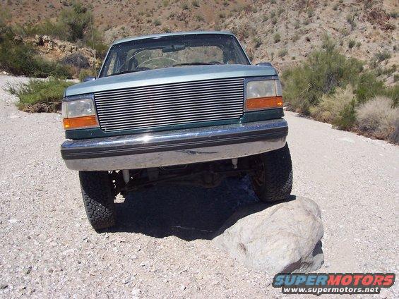 Green SUV with a chrome grille driving over a rock on a dirt road