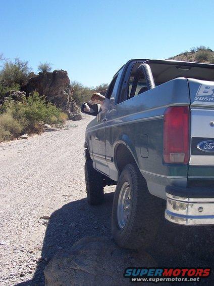 1996 Ford Bronco rear view driving on a rocky dirt road with a dog in the window