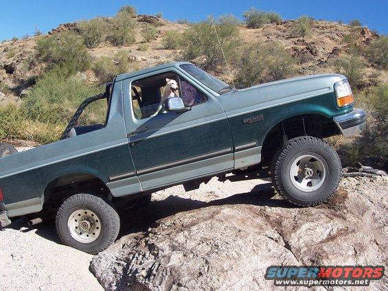 Two-tone green 1996 Ford Bronco on rocky terrain with a dog in the driver's seat