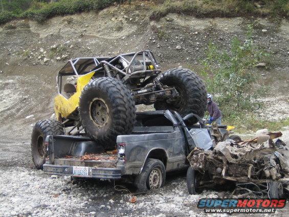 Yellow off-road buggy on top of a wrecked pickup truck. Another wrecked vehicle is to the right