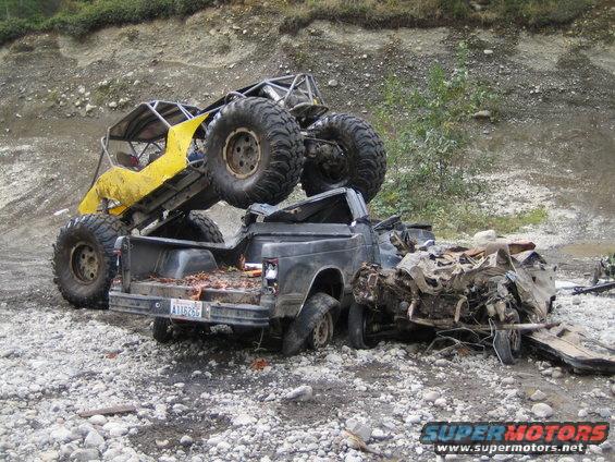 Yellow off-road buggy on top of a wrecked pickup truck. Pickup truck is heavily damaged