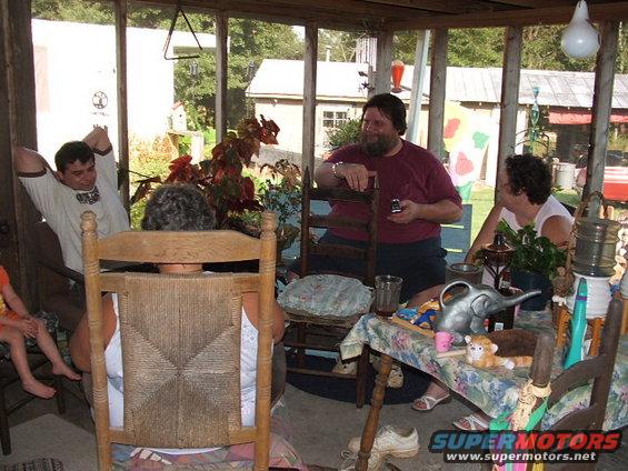 People gathered on a screened porch with tables and chairs, with a "SUPERMOTORS.NET" watermark visible