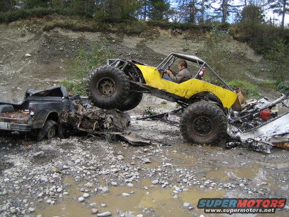Yellow buggy on wrecked black truck in muddy terrain