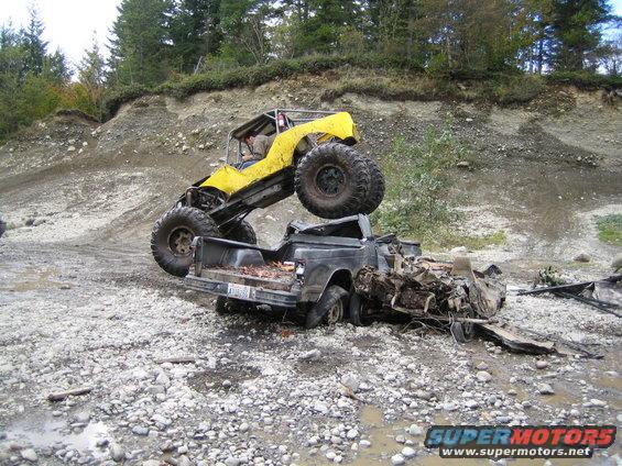 Yellow buggy atop wrecked pickup truck in rocky terrain