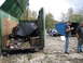 1990 Ford Bronco - A dumpster is overflowing with garbage, while two men stand near a car and a large blue container in the background.