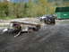 1990 Ford Bronco - A black SUV tows a heavily damaged trailer through a muddy area, with a white truck and green dumpsters in the background.