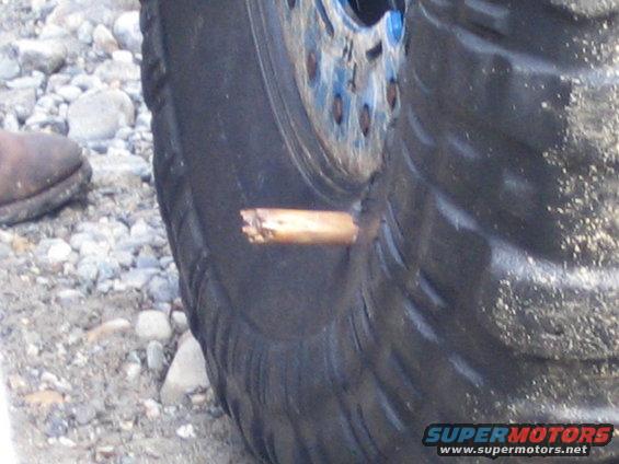 Close-up of a tire with a wooden object stuck in it. A person's boot is visible to the left