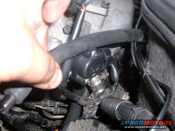 Close-up of a hand near a black sensor attached to hoses and wiring in an engine bay
