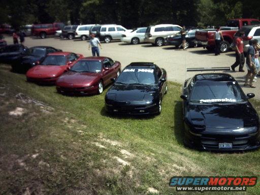 Three black Ford Probes and two red Ford Probes parked on grass and asphalt