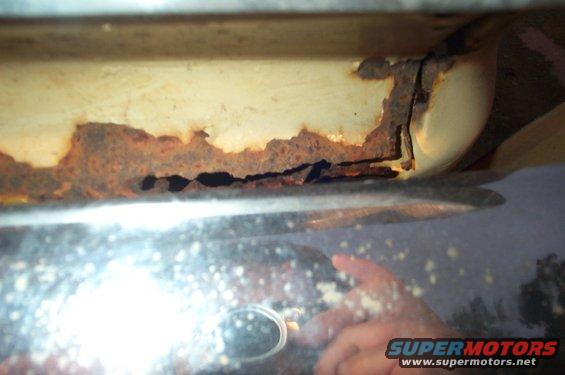 Close-up of heavily rusted metal panel with a shiny surface below reflecting light and a hand