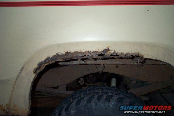close-up of heavily rusted rear wheel well on a cream-colored vehicle with red trim above