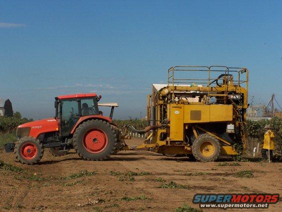 Red tractor pulling yellow harvesting machine in a field
