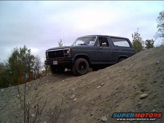 Dark SUV on a dirt incline, front grille visible, cloudy sky