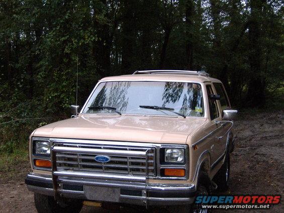 Tan Ford Bronco with chrome grille and roof rack, parked on a dirt road
