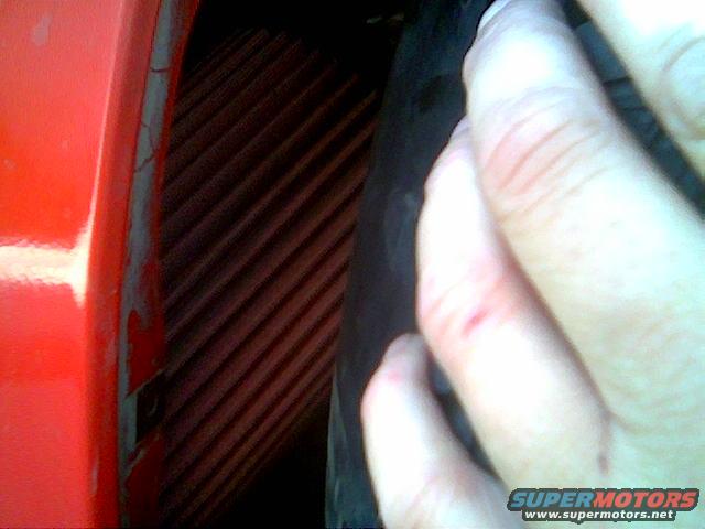 Red car panel next to a tire and a hand with cuts