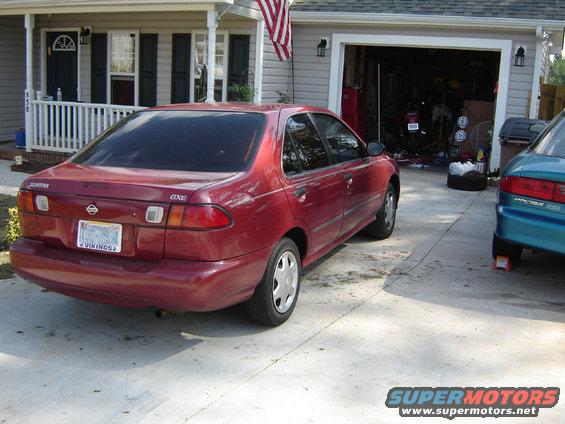 Red 1998 Nissan Sentra parked in driveway next to a teal car. House and garage in background
