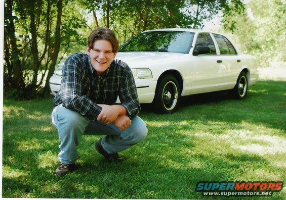 White 2000 Ford Crown Victoria 3/4 front view with a person crouching in front