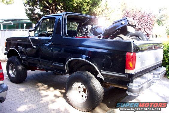Black 1990s Ford Bronco with lifted suspension, carrying a motorcycle in its bed