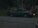 1996 Ford Probe - A dark gray coupe is parked on the side of the road near a park.