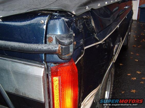 Rear corner of dark blue SUV with soft top, showing damage and a red taillight