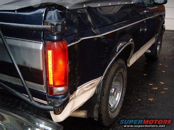 1993 Ford Bronco rear quarter panel, taillight, and tire. Dark blue paint with white trim