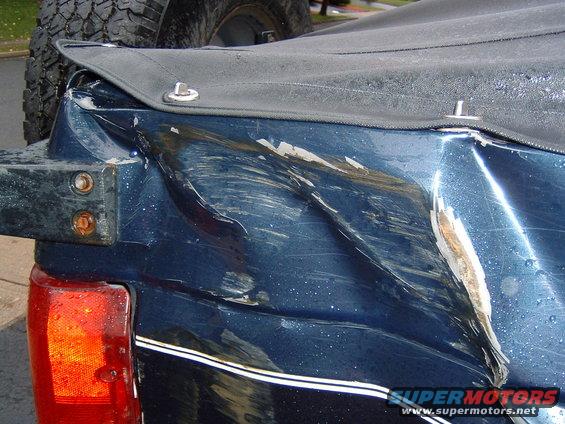 Rear quarter panel of a dark blue SUV with significant damage, showing scraped paint and denting