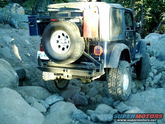 Black Jeep Wrangler TJ on rocky trail with spare tire and gas can