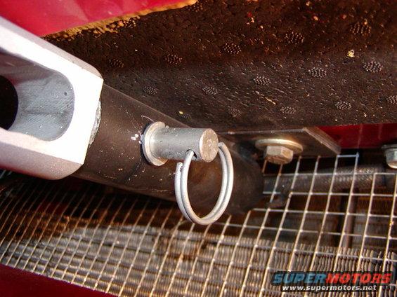 Close-up of a metal bracket and pin assembly attached to a black hose, with a wire mesh radiator visible below