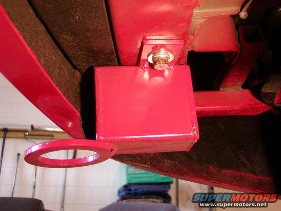 Red metal tow hook assembly bolted to vehicle frame, viewed from below