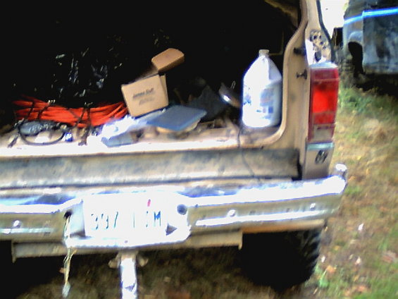 Back of a tan pickup truck with stuff in the bed, another vehicle is visible to the right