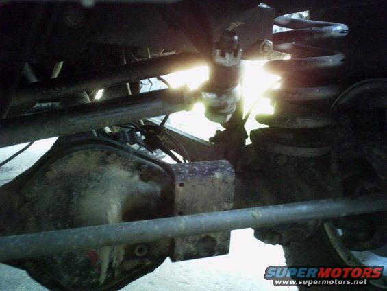 Underside of a vehicle showing the rear differential, suspension spring, and steering linkage