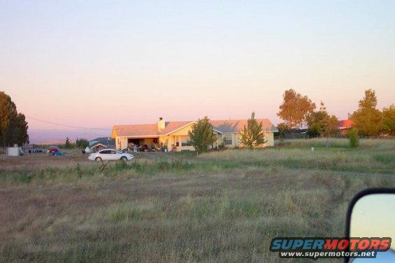 White sedan parked in front of a rural house at sunset