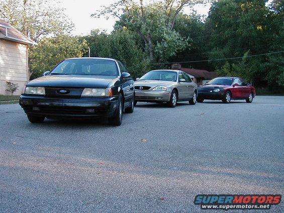 1990 Ford Taurus parked in front, with a gold sedan and a red sports car behind it
