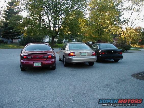 Red sedan, gold sedan, and black sedan parked in a lot. Red sedan has a license plate reading 'EE V 4438'