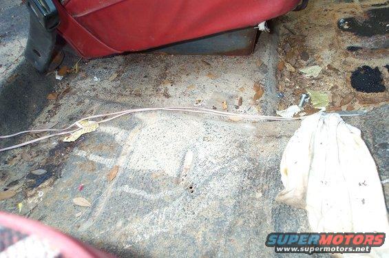 Interior floor of a vehicle with red seat, debris, and wiring