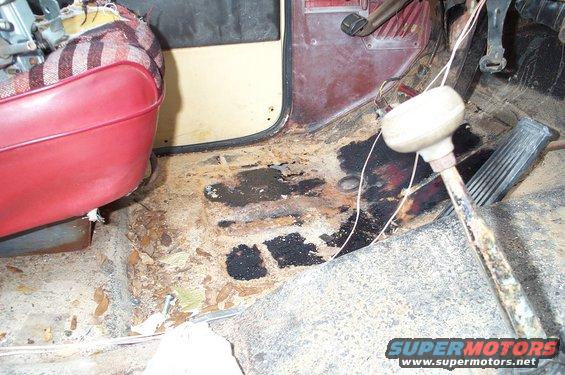 driver's side floorboard with rust and debris, red seat visible
