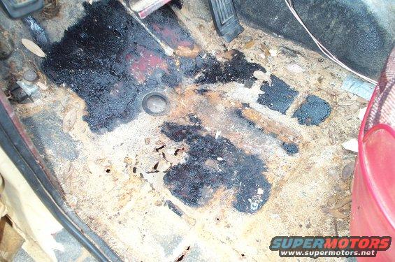 Vehicle interior floor with rust, black tar-like substance, and debris