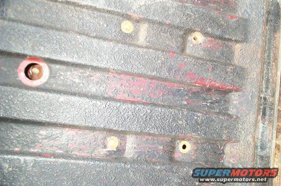 Close-up of a truck bed with tie-down points and some red paint showing through the black coating