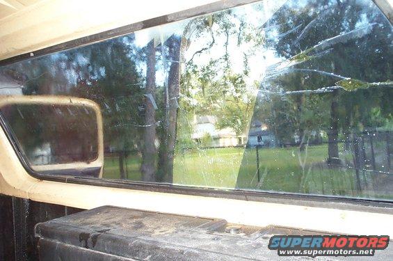 Interior view through cracked rear window of a truck, showing trees and a house outside