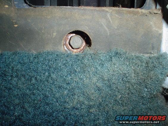 Close-up of a rusty bolt through teal carpet in a vehicle interior
