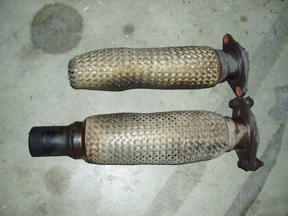 Two exhaust flex pipes with braided metal sleeves and flange connectors on a concrete surface