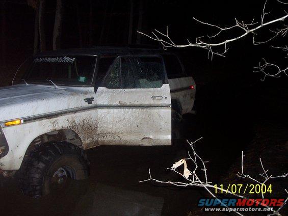 White 1979 Ford Bronco with open door, covered in mud