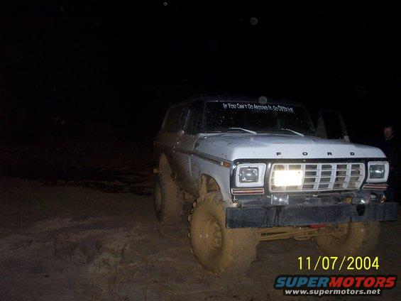 White 1979 Ford Bronco with mud on tires and body, parked at night