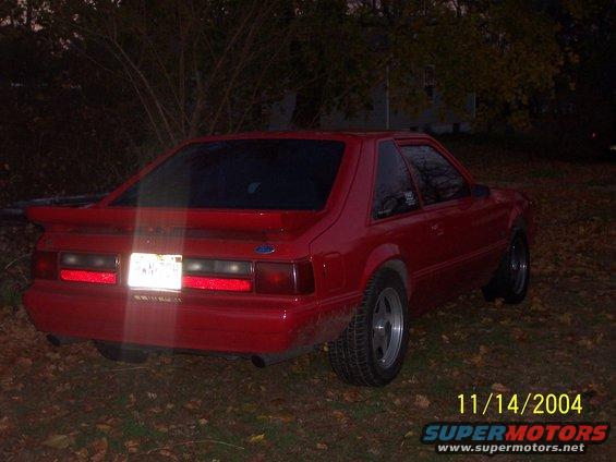 Red coupe with a spoiler and tinted windows parked on grass with fallen leaves