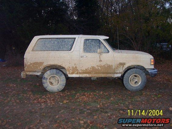 White SUV covered in mud, side view. Appears to be a 1980s Ford Bronco